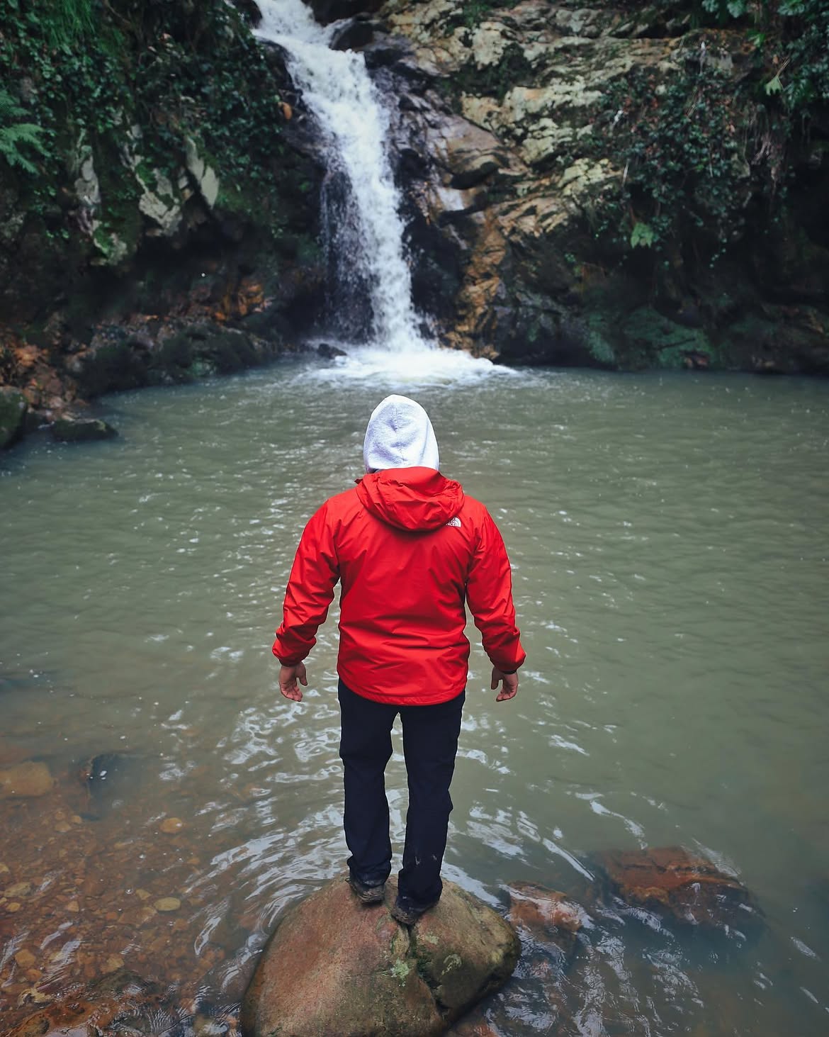 Person facing a waterfall in a red jacket