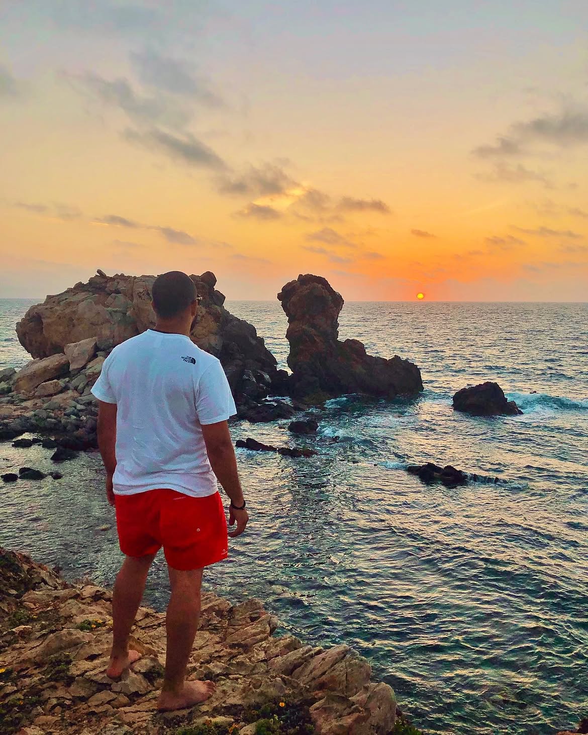 Person standing at the rocky coast at sunset