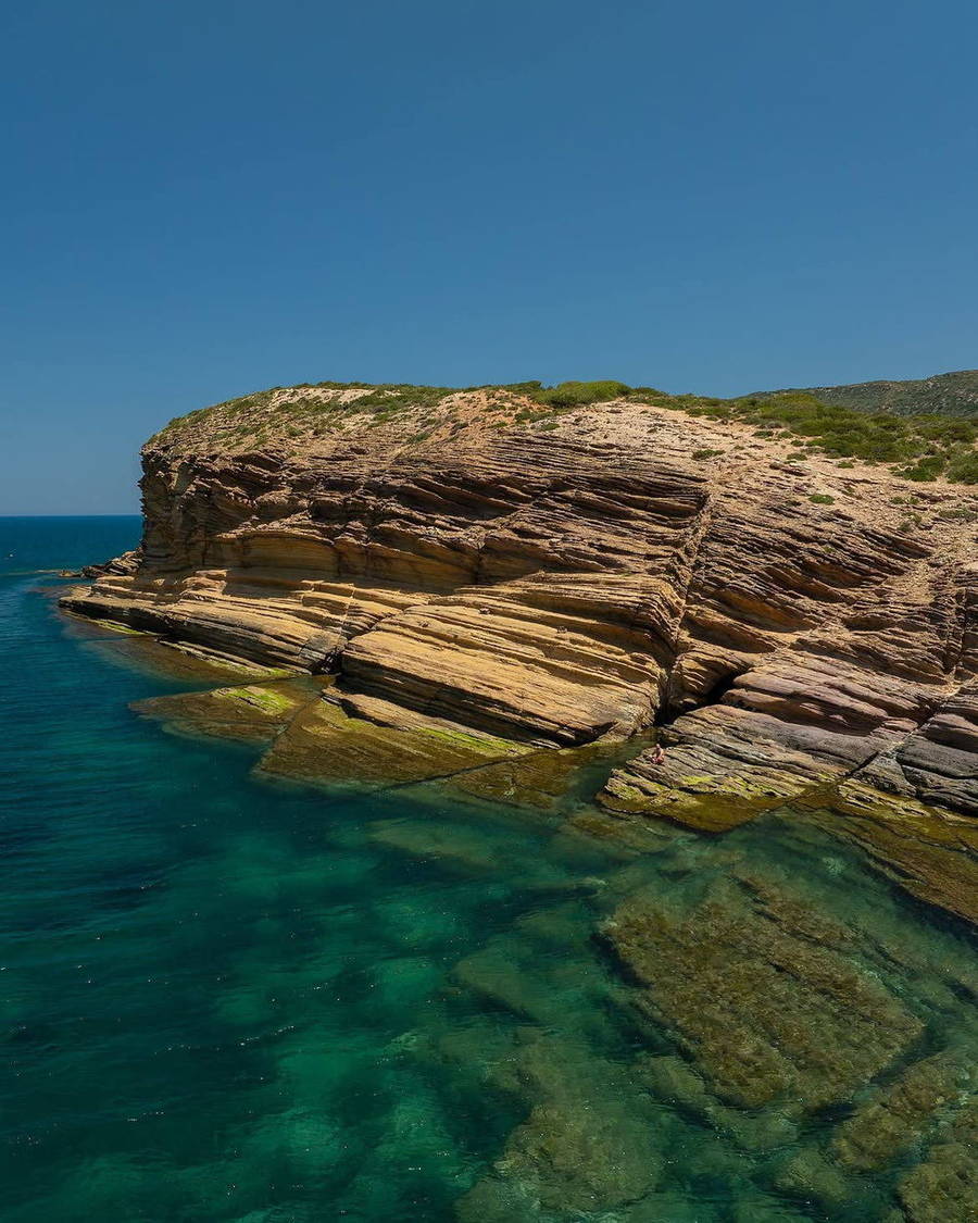 Layered rocky coastline above clear turquoise water