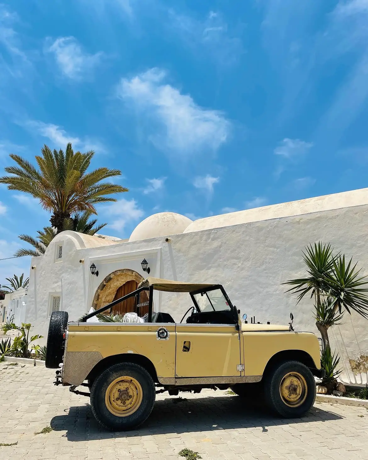 A classic yellow Land Rover beside a white island house